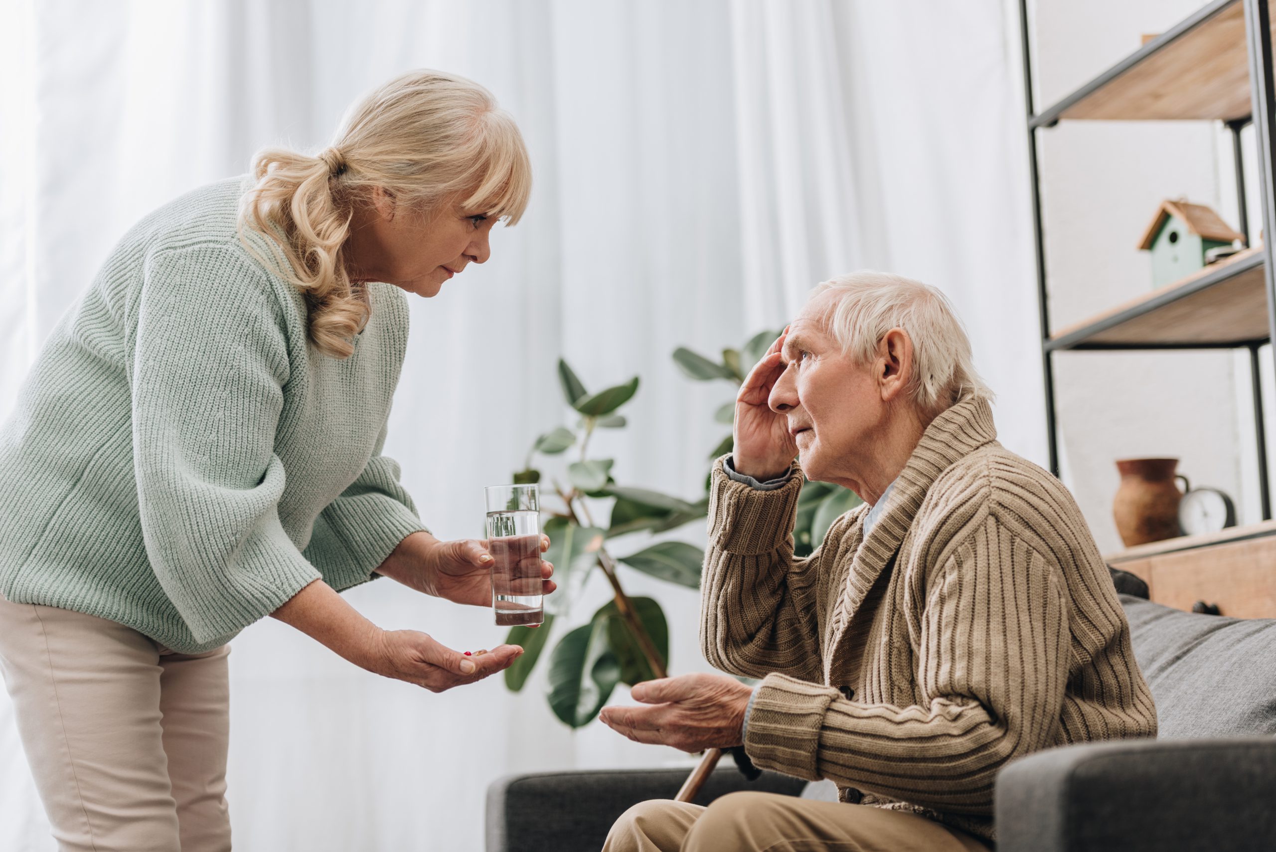 senior woman giving pills and glass of water to old man with wal