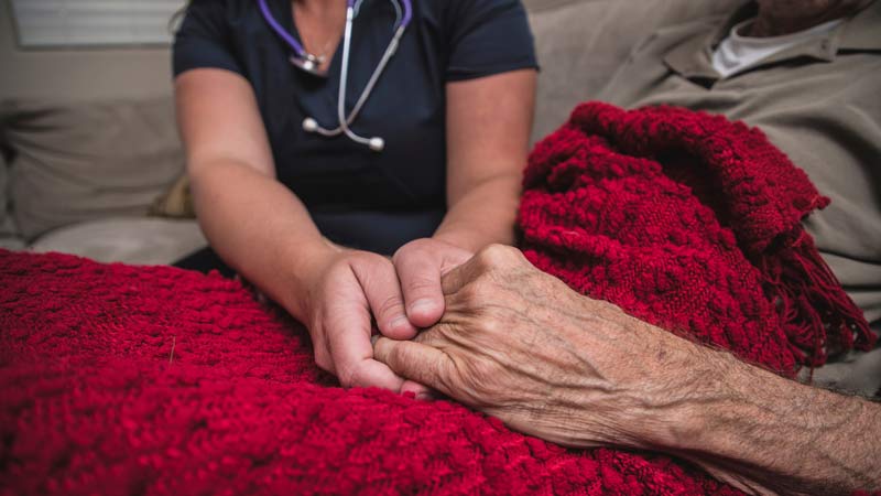 Care giver holding hands of a patient covered with red blanket